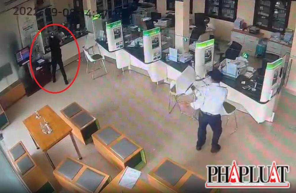 Tên cướp (khoanh tròn đỏ) dùng súng khống chế nhân viên ngân hàng và bảo vệ. Ảnh: VH