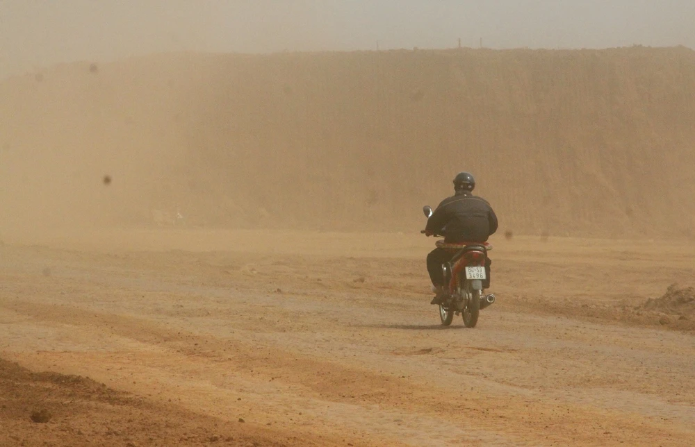 Một người đàn ông đi xe máy gắng vượt qua "bão" bụi tại khu vực dự án.