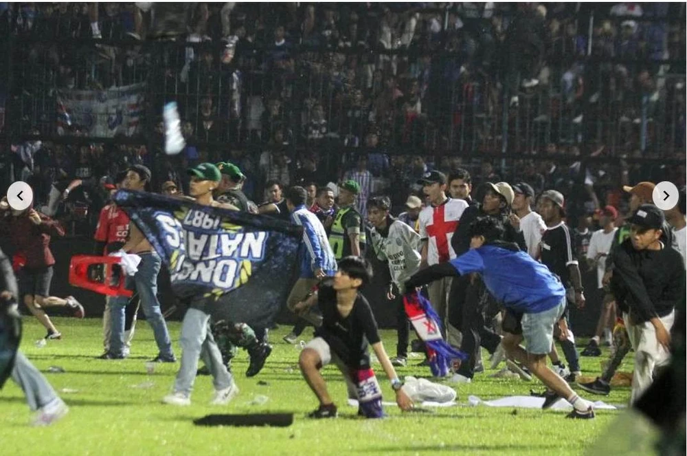 Fan chủ nhà Arema FC gây hấn trước tiên. Ảnh: AFP Trên khán đài thì lửa cháy, dưới sân thì... hỗn loạn. Ảnh: AFP Cảnh sát dùng súng bắn hơi cay để ngăn chặn đám đông. Ảnh: AFP