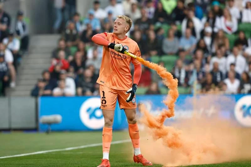 Thủ môn Tom Glover của Melbourne City đã lượm ném quả pháo sáng ra ngoài. Bạo động không phải xuất phát từ tính chất căng thẳng trận derby Melbourne. ... mà do ban tổ chức A-League đưa vòng chung kết của giải đấu này về Sydney ba mùa liên tiếp khiến fan Melbourne cay cú. Họ cáo buộc rằng, ban tổ chức A-League đã ăn tiền bẩn để đưa vòng chung kết A-League về Sydney ba mùa liên tiếp. Vụ lộn xộn này xuất phát từ một fan la lớn phản đối sau đó nhanh chóng lan rộng ra. Fan tràn xuống sân phá rồi đu người lên cả cầu môn.