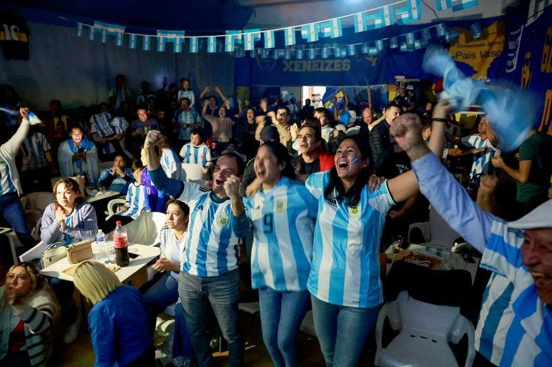 Fan Argentina ăn mừng ở trung tâm Văn hóa Guernica ở Tây Ban Nha. Ảnh: Reuters. "Messi" có mặt ở Madrid ăn mừng chiến thắng. Ảnh: Reuters Người phụ nữ bán hàng trong chợ ở Argentina bật khóc khi Di Maria ghi bàn thứ hai cho Argentina. Ảnh: Reuters Ở trung tâm Tampines, Singapore, fan Argentina ăn mừng. Ảnh: S.T Singapore lập các trung tâm truyền hình trực tiếp để phục vụ người dân và cả người nước ngoài công tác và du lịch ở Singapore xem. Ảnh: S.T Các fan chúc mừng nhau khi Messi mở điểm từ chấm 11m, đây là hình ảnh tại Lo De Diego, Argentina. Ảnh: Reuters Tại thủ đô Buenos Aires của Argentina...mọi người thức dậy xem chung kết và ăn mừng. Ảnh: Reuters Tại một trung tâm văn hóa ở Buenos Aires. Ảnh: Reuters ...Còn trên sân Lusail, nơi diễn ra trận chung kết có khoảng 10 ngàn người Argentina, không kể fan của Argentina. Ảnh: Reuters
