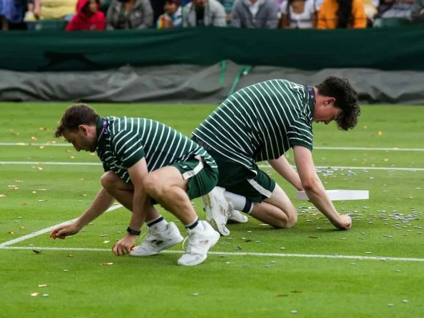 Sang ngày thi đấu thứ năm cũng trên sân 18, những người hoạt động môi trường mặc áo phông với dòng chữ Just Stop Oil tiếp tục rải giấy kim tuyến lên mặt sân, lúc đó đang diễn ra trận đấu Katie Boulter và Daria Saville khiến trận đấu hoãn. Ảnh: S.E Những người vào sân quậy phá bị lực lượng chức năng trong sân bắt giữ và kéo ra khỏi sân. Ảnh: S.E Những mảnh giấy kim tuyến cực mỏng dính vào cỏ rất tốn công "gỡ từng sợi". Ảnh: S.E Giá cả leo thang, lạm phát khiến tình hình xã hội căng thẳng, nay lại bỏ dầu dùng than và khí gas sẽ gây ô nhiễm môi trường, những người phản đối lập luận như thế. Ảnh: S.E