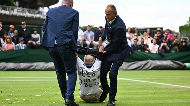 Ngày thi đấu thứ ba của Wimbledon, những nhà hoạt động bảo vệ môi trường rải những mảnh kim tuyến lên mặt sân cùng lúc với trời mưa. Điều đó khiến trận đấu giữa Dimitrov và Shimabukuro phải hoãn, để nhân viên dọn dẹp những giấy kim tuyến cuốn vào cỏ rất khó gỡ. Ảnh: S.E Sang ngày thi đấu thứ năm cũng trên sân 18, những người hoạt động môi trường mặc áo phông với dòng chữ Just Stop Oil tiếp tục rải giấy kim tuyến lên mặt sân, lúc đó đang diễn ra trận đấu Katie Boulter và Daria Saville khiến trận đấu hoãn. Ảnh: S.E Những người vào sân quậy phá bị lực lượng chức năng trong sân bắt giữ và kéo ra khỏi sân. Ảnh: S.E Những mảnh giấy kim tuyến cực mỏng dính vào cỏ rất tốn công "gỡ từng sợi". Ảnh: S.E Giá cả leo thang, lạm phát khiến tình hình xã hội căng thẳng, nay lại bỏ dầu dùng than và khí gas sẽ gây ô nhiễm môi trường, những người phản đối lập luận như thế. Ảnh: S.E