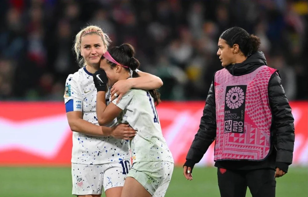 Bà chị đội trưởng Lindsey Horan vỗ về cô em gái Sophia Smith, 21 tuổi, người đá hỏng quả luân lưu trong loạt sút năm quả. Ảnh: SMH. Hai "tội đồ" của tuyển Mỹ sút hỏng phạt đền trong loạt sút 5 quả gồm bà chị cả Megan Rapinoe và Sophia Smith. Ảnh:SMH World Cup 2019, Rapinoe có hai danh hiệu cá nhân gồm cầu thủ xuất sắc nhất giải và vua phá lưới (5 bàn), bốn năm sau phong độ của cô đã xuống ở tuổi 37, ít ra sân. Ảnh: SMH. Rapinoe...cắn rứt vì mình sút hỏng phạt đền. Ảnh: SMH Các tuyển thủ Mỹ an ủi nhau sau khi chính thức thành cựu vô địch sau loạt luân lưu thứ 7. Ảnh: SMH. Thủ môn Naeher quờ quạng trước cú sút của Hurtig ở loạt sút thứ bảy, bóng đã qua vạch vôi...1mm. Ảnh: SMH. Sau khi trọng tài Stephanie Frappart công nhận bàn thắng ở loạt luân lưu quyết định, Hurtig ăn mừng cùng đồng đội vào tứ kết. Ảnh: SMH.