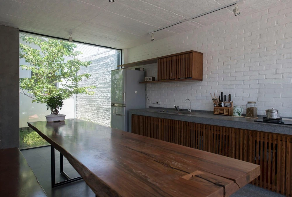 Bếp và bàn ăn bên cạnh khoảng thông tầng có trồng cây xanh khiến không gian này nhận được lượng ánh sáng vừa phải.