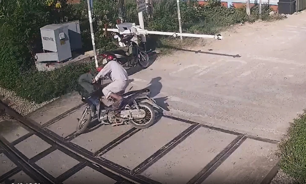 Người đàn ông đi xe máy cố vượt qua đèn đỏ, rào chắn và chuông báo hiệu khi tàu hỏa đang lao tới và nữ nhân viên đường sắt lao tới kéo ra. Ảnh: Cắt từ clip