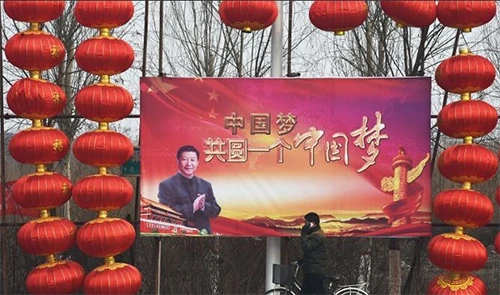 n walks past a billboard featuring a photo of Chinese President Xi Jinping beside lantern decorations for the Lunar New Year in Baoding, China's northern Hebei province. The Chinese characters read