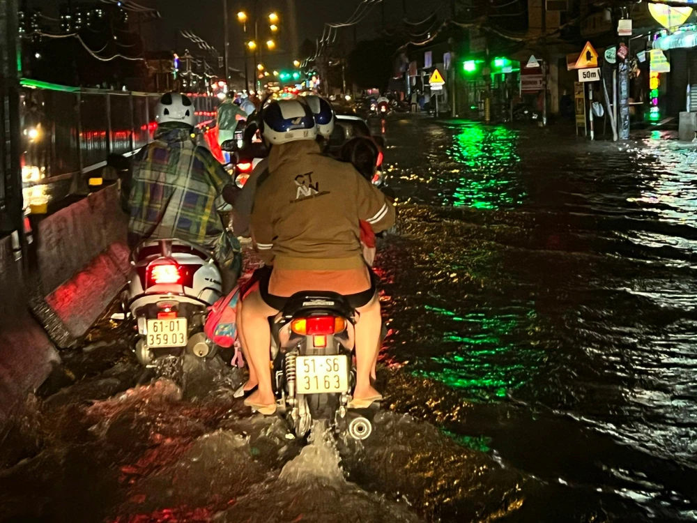 Nước ngập sâu nghiêng về phía lề đường khiến người đi xe máy phải chèn ra phần đường dành cho ô tô. Ảnh VÕ TÙNG