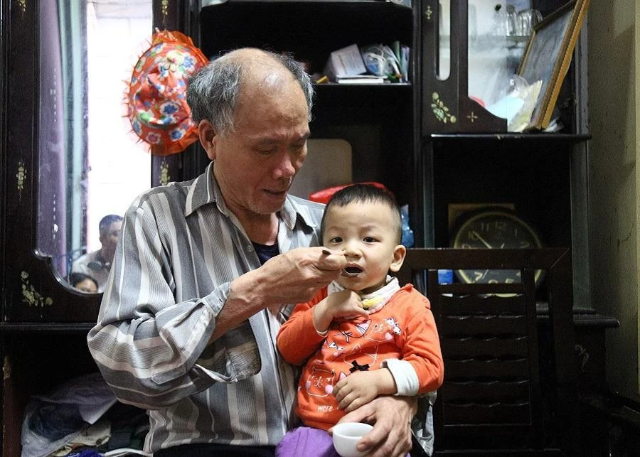 Ông Châu một mình chăm đứa cháu út, vợ và con trai nằm liệt một chỗ. Ảnh: UYÊN TRANG