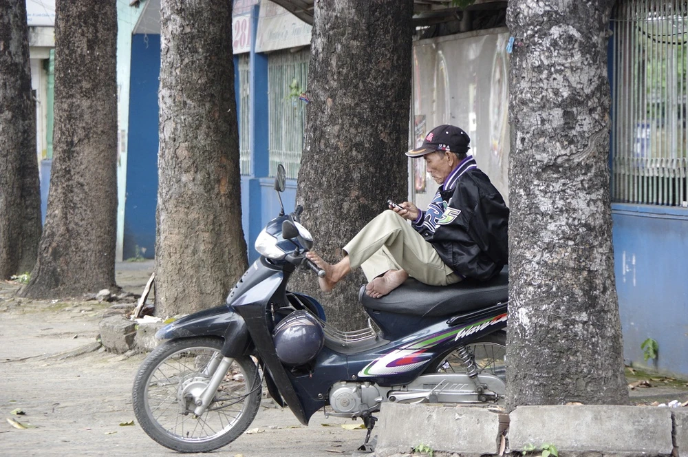 Chú Bảy, chạy xe ôm trên đường Võ Văn Ngân, quận Thủ Đức ngồi thu mình trong hàng cây. 