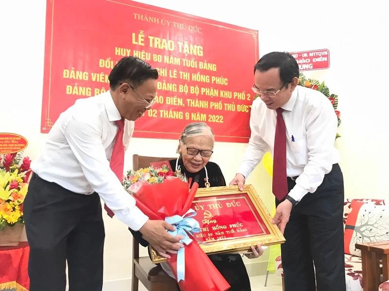 Bí thư Thành ủy TP.HCM Nguyễn Văn Nên và Bí thư Thành ủy TP Thủ Đức Nguyễn Hữu Hiệp trao huy hiệu, hoa chúc mừng cho bà Lê Thị Hồng Phúc. Ảnh: THANH TUYỀN