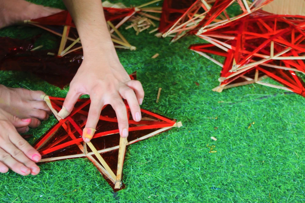 Con chị Thu phụ ba mẹ dán giấy cho lồng đèn. Ảnh: THẢO PHƯƠNG