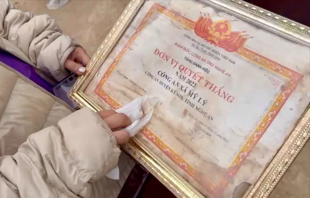 Một thành viên đoàn thiện nguyện cẩn thận lau sạch bằng khen trước khi trao trả lại cho Công an xã Mỹ Lý
