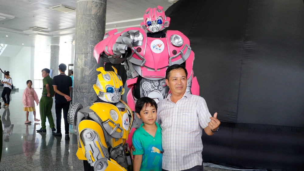 Các em học sinh và phụ huynh chụp ảnh lưu niệm với robot tại sự kiện Tuần lễ NASA Việt Nam. Ảnh CHÂU ANH