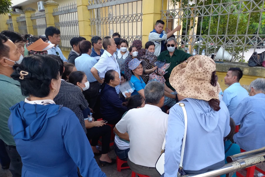 Một số người dân ngồi ở vỉa hè theo dõi phiên tòa qua loa phóng thanh.