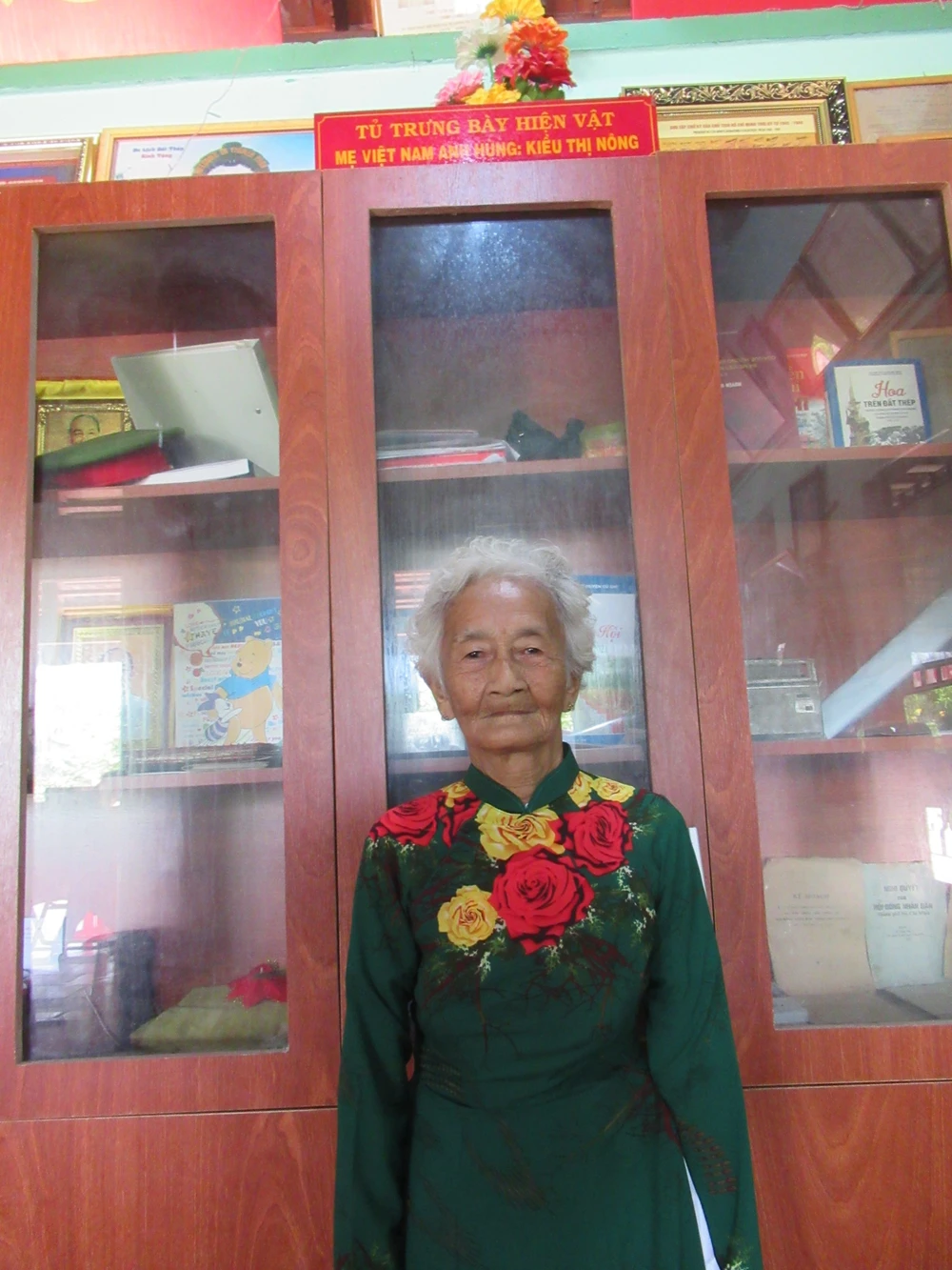 Mẹ Kiều Thị Nông bên tủ trưng bày hiện vật. Ảnh: YC Mẹ Kiều Thị Nông bên tủ trưng bày hiện vật. Ảnh: YC