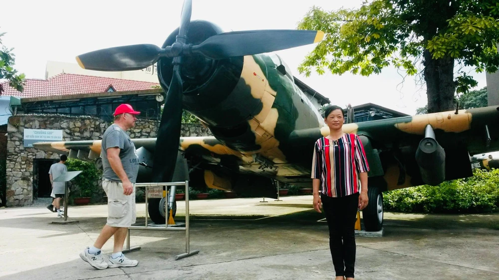 Chị Nguyệt chụp hình lưu niệm với hiện vật trong khuôn viên bảo tàng. Ảnh: PHƯƠNG LÊ.