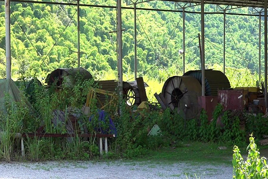 Máy móc nằm im lìm giữa cỏ dại trong nhà xưởng.