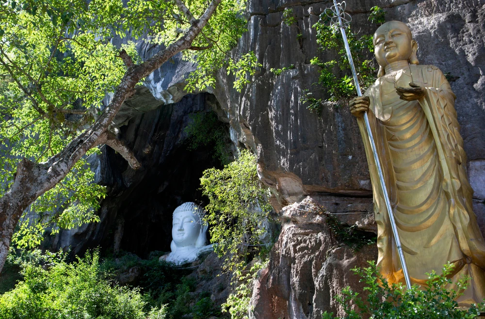 Cùng nằm trong hệ thống động ở Tiên Sơn, còn có động Ngọc Kiều với cửa động rộng lớn có đá bắc ngang qua tựa cây cầu Ngọc nên mới có tên như vậy. Từ dưới nhìn lên, tầng cửa động một tượng Phật lớn ẩn hiện giữa những tàng cây xanh mát. Ảnh: ĐẶNG TRUNG