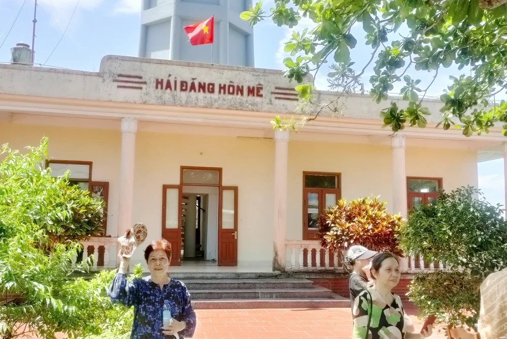 Những du khách tranh thủ lưu lại khoảnh khắc dưới chân ngọn hải đăng trên đảo Hòn Mê. Ảnh: ĐẶNG TRUNG