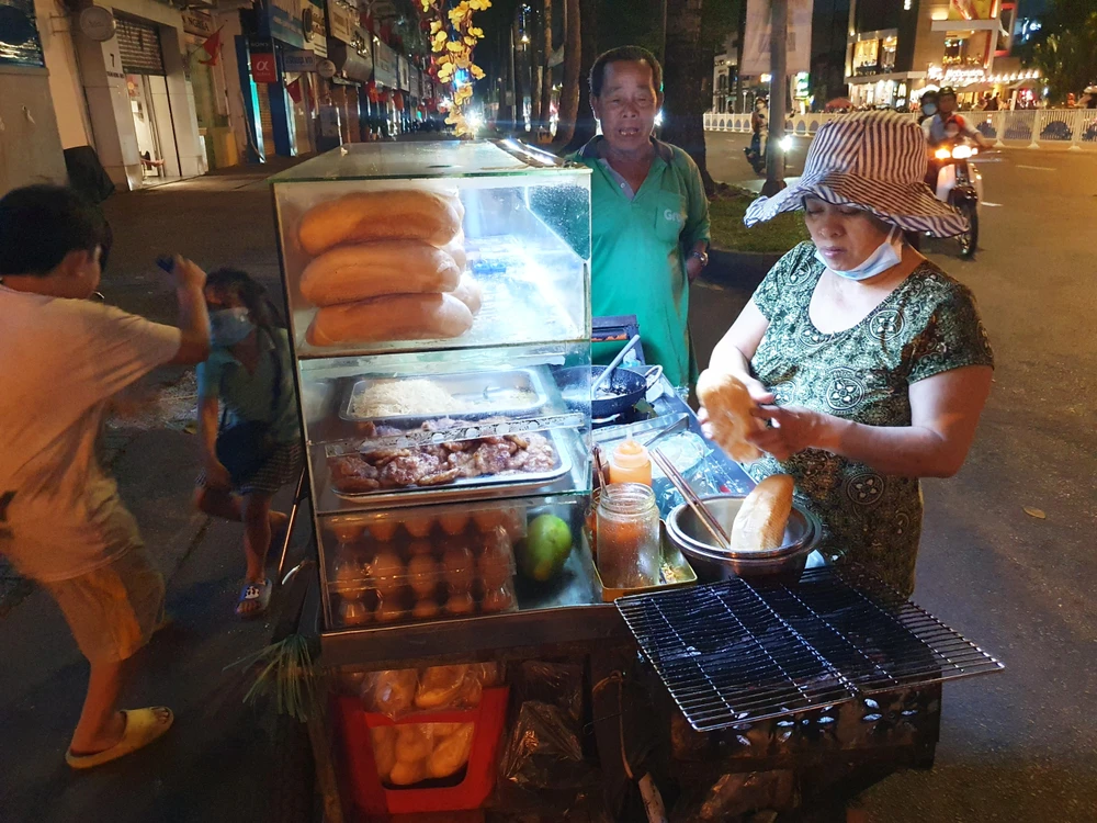 Chị Hiền đang đẩy xe bán bánh mì trên đường Trần Hưng Đạo, quận 1, 2 con nhỏ luôn đi theo cùng chị. "Mình bán hàng rong, cũng ráng bán thêm chút nào hay chút đấy dịp giao thừa, ráng cho 2 đứa nhỏ đi học. Bình thường sáng 2 đứa học, chiều tối phụ mẹ bán thêm", chị Hiền chia sẻ.