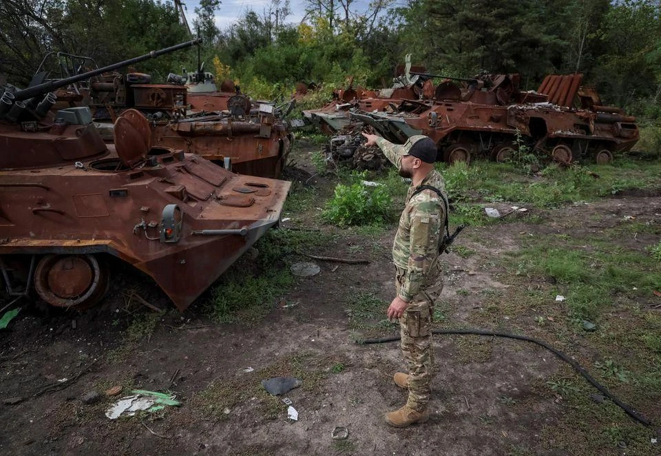 Lính Ukraine xem xét những chiếc xe thiết giáp của Nga bị phá hủy ở TP Izium, tỉnh Kharkiv. Ảnh: REUTERS