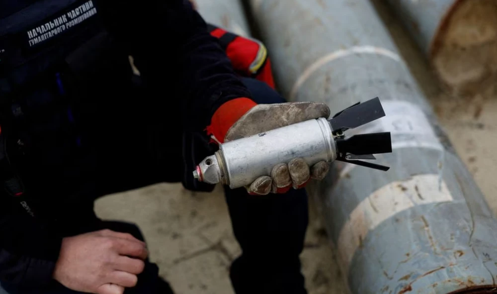 Lính Ukraine cầm một quả bom chùm đã bị vô hiệu hóa trong khu trưng bày các mảnh tên lửa do quân Nga sử dụng tại tỉnh Kharkiv hồi tháng 11-2022. Ảnh: REUTERS