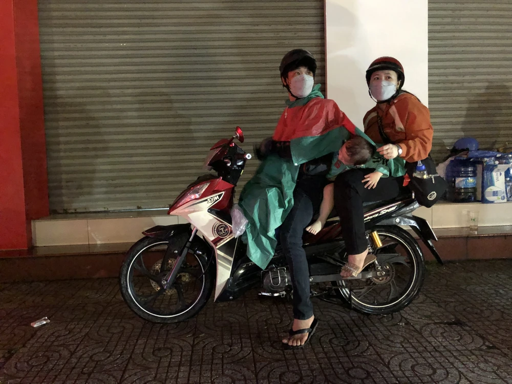 Nhiều gia đình có con nhỏ phải tấp vào nhà dân ven đường để đợi tạnh mưa tiếp tục đi tiếp. Ảnh: HUỲNH DU