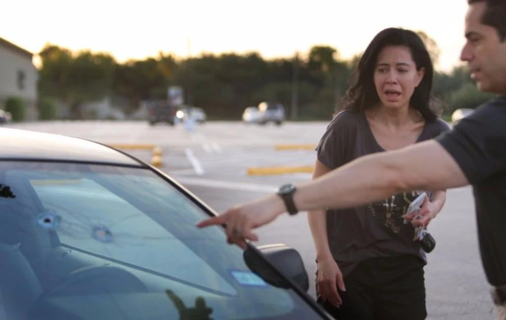 Người chồng đang chỉ cho vợ mình những vết đạn thủ phạm bắn vào xe mình trong vụ xả súng. 