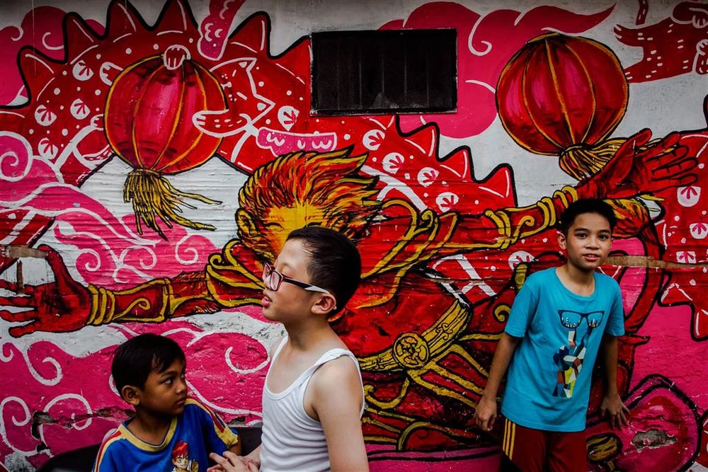 Các cậu bé Indonesia vui chơi trước bức tranh tường đón năm mới ở thị trấn Surabaya, Đông Java (Indonesia) ngày 30 Tết, nhằm ngày 27-1. Ảnh: EPA