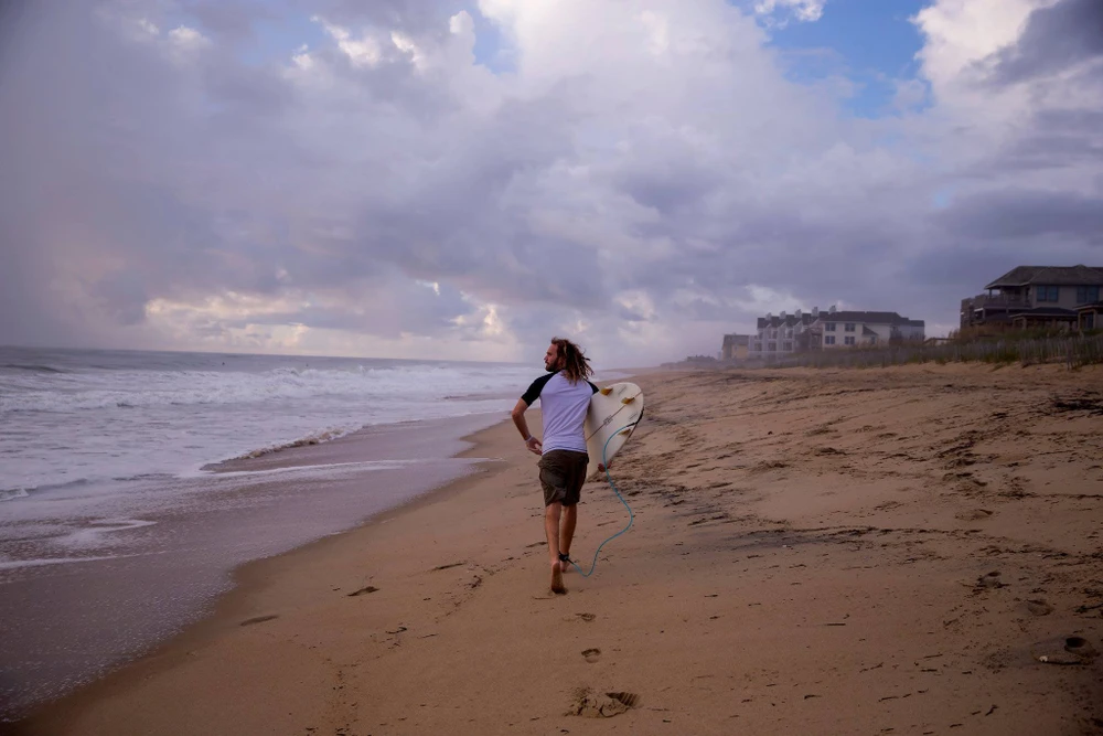 Dù có cảnh báo bão, có người vẫn bình tĩnh đi lướt sóng tại thị trấn Kill Devil Hills, hạt Dare, bang North Carolina (Mỹ) ngày 12-9. Ảnh: NEW YORK TIMES