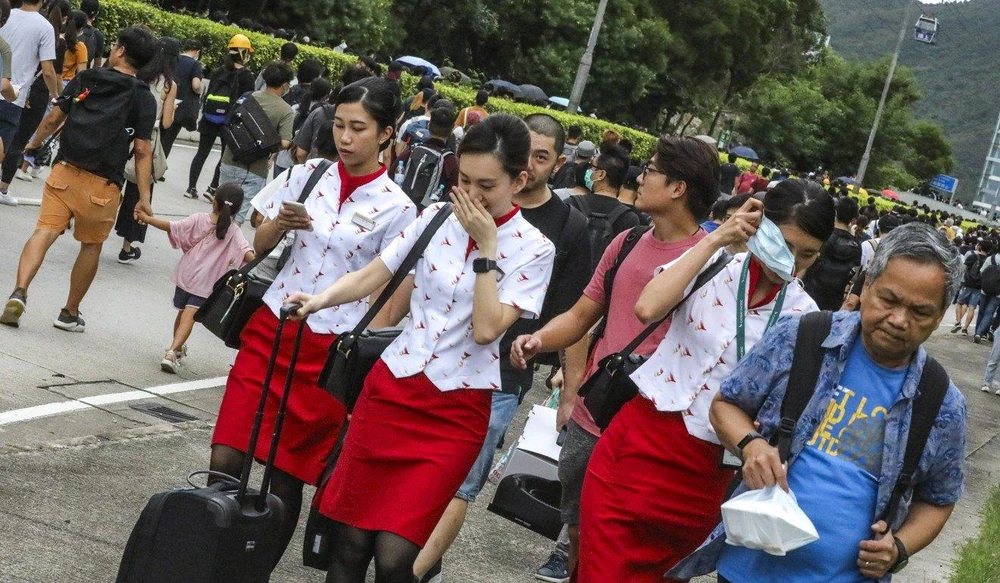 Hành khách và phi hành đoàn kéo hành lý đi bộ về sân bay. Ảnh: SCMP
