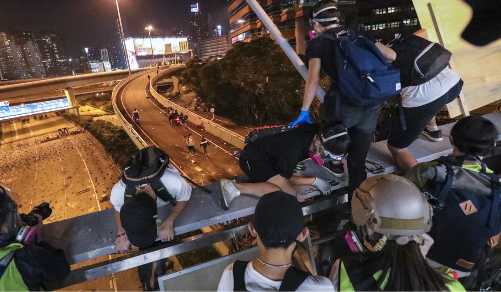 Người biểu tình đu dây thoát từ một cây cầu đi bộ xuống đường và được xe máy chở đi. Ảnh: SCMP