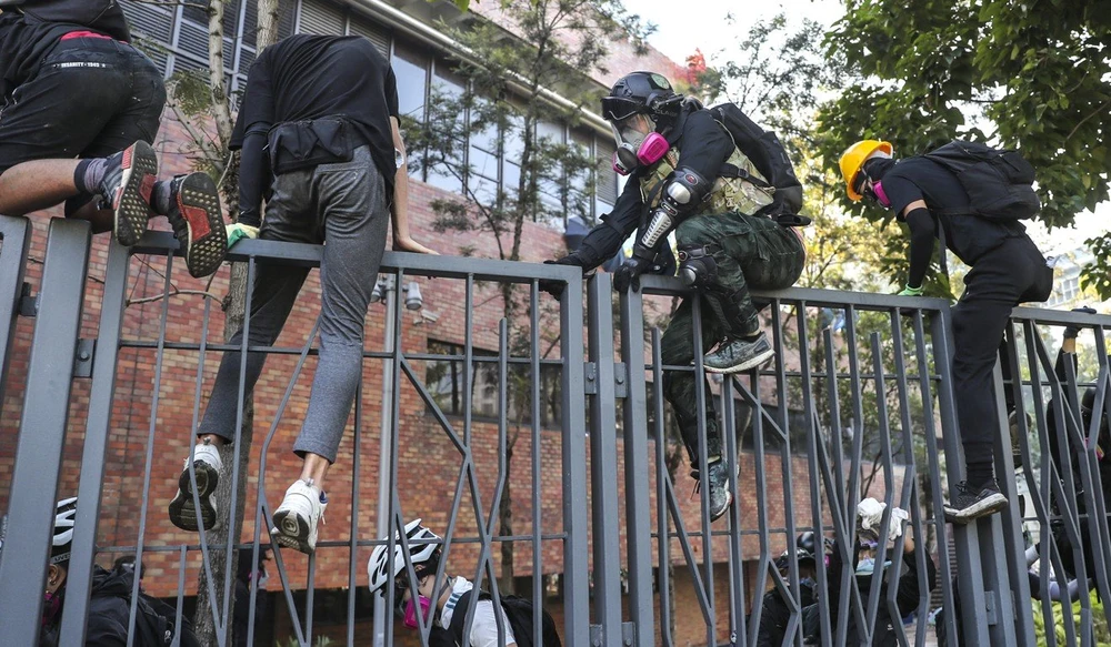 Nhiều sinh viên trèo hàng rào cố gắng rời trường. Ảnh: SCMP