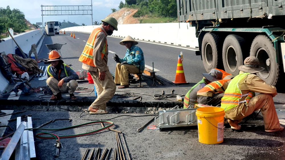 Các công nhân thi công bên dòng phương tiện lưu thông với tốc độ cao. Công nhân cho biết đang lắp các khe co giãn trên cao tốc.