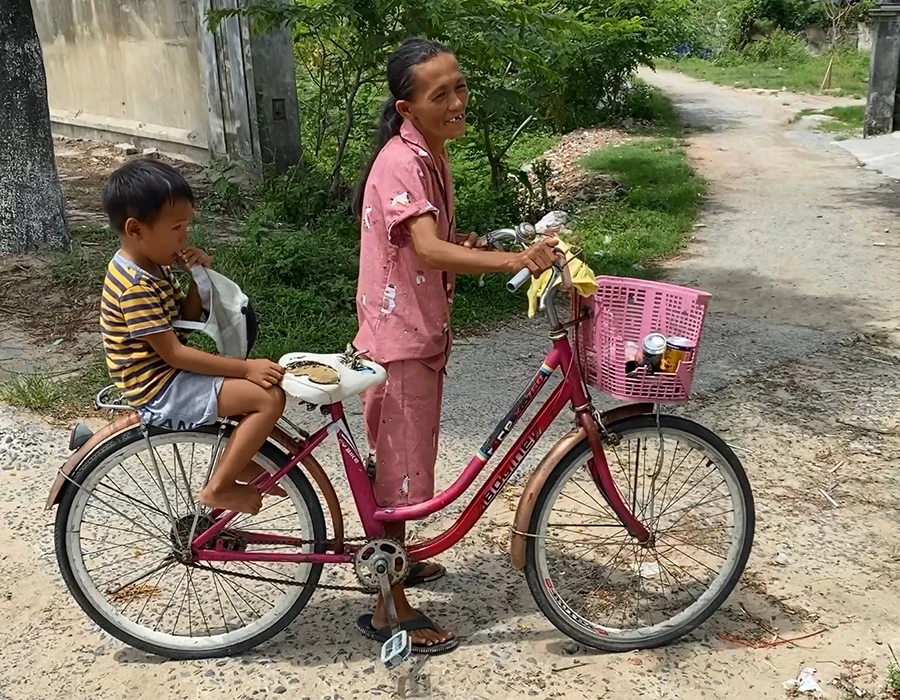 Người vợ biết chạy xe đạp chở con đi lấy thực phẩm sống về nấu ăn cho cả nhà, không còn cảnh tìm được gì thì ăn nấy. Ảnh: HẢI HIẾU