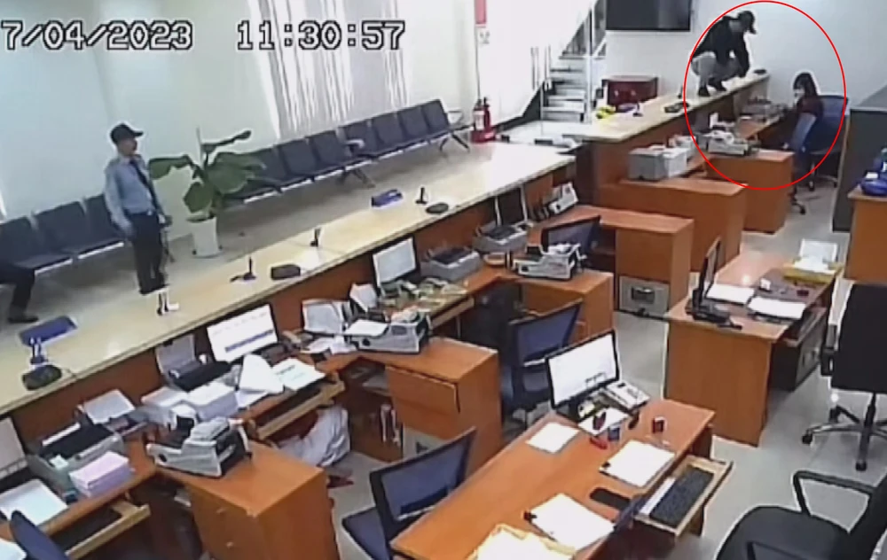 Tên cướp leo lên quầy của ngân hàng dùng súng uy hiếp bắt nữ nhân viên đưa tiền. Ảnh: Cắt từ camera