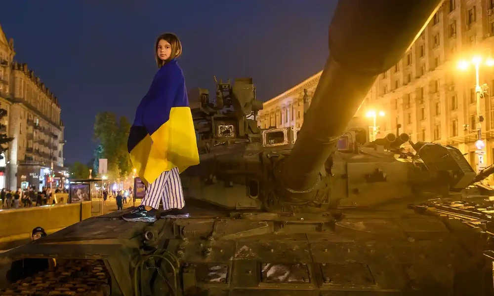 Bé gái Ukraine đứng trên một xe tăng của Nga bị phá hủy ở thủ đô Kiev. Ảnh: REUTERS