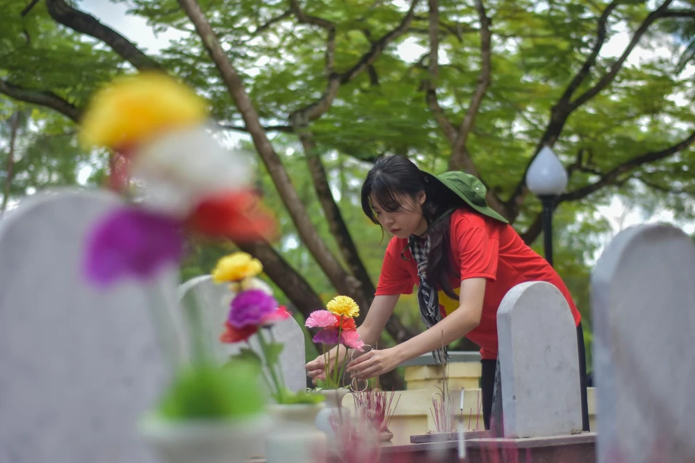 Một nữ sinh chỉnh sửa lại những bông hoa trên mộ của các liệt sĩ. Ảnh: NGUYỄN DO