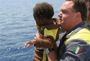 Một sĩ quan thuộc lực lượng tuần duyên Italy cứu một em bé nhập cư người châu Phi sau một tai nạn chìm tàu trên Địa Trung Hải. Ảnh: AFP.