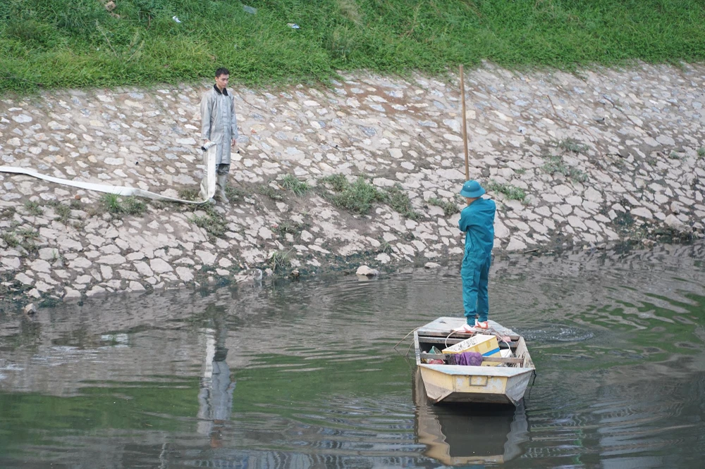 Dây được bắc ngang qua sông Tô Lịch để đấu vòi vào một chiếc xe cứu hoả đang chờ ở phía bờ bên.