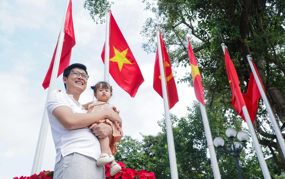 Hình ảnh người cha chụp ảnh lưu niệm cùng con gái bên lá cờ tổ quốc tại khu vực chân tượng đài Lý Thái Tổ.