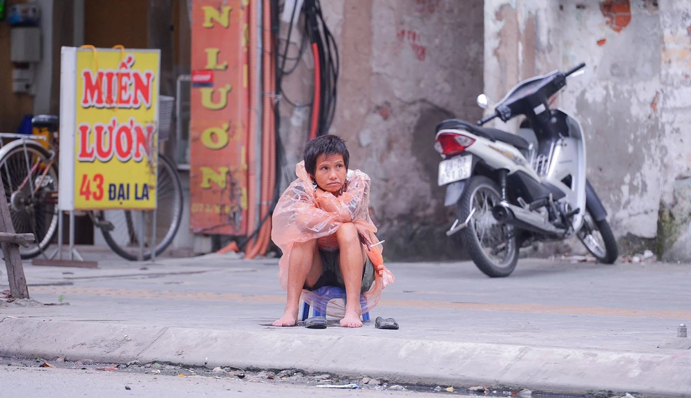 Trên phố Đại La, một người lao động mặc áo mưa ngồi co ro vì lạnh.