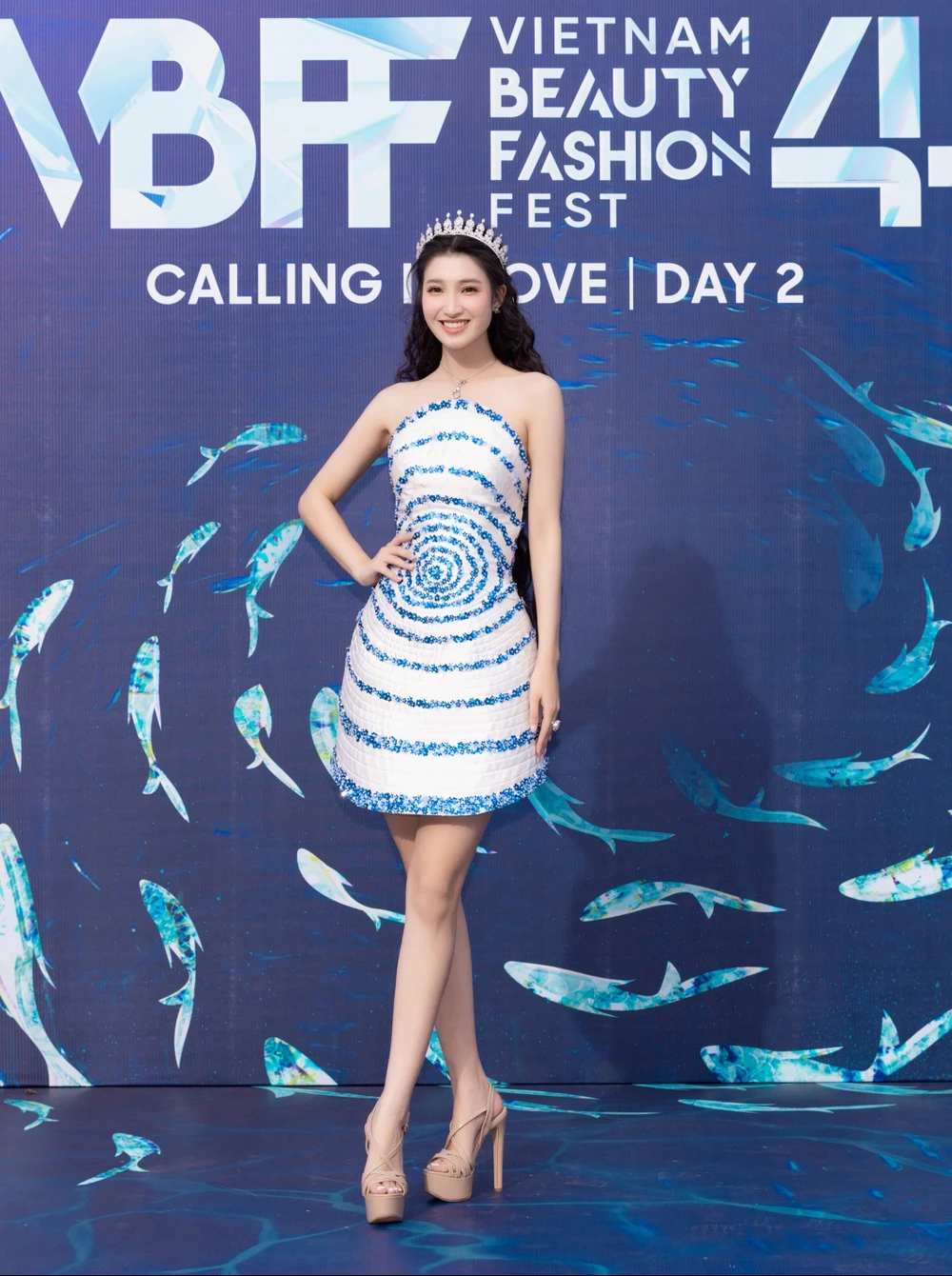 Á hậu Phương Nhi chọn diện chiếc váy cocktail cúp ngực màu trắng, điểm nhấn là những họa tiết kim tuyến lấp lánh tạo hiệu ứng sóng nước bắt mắt.