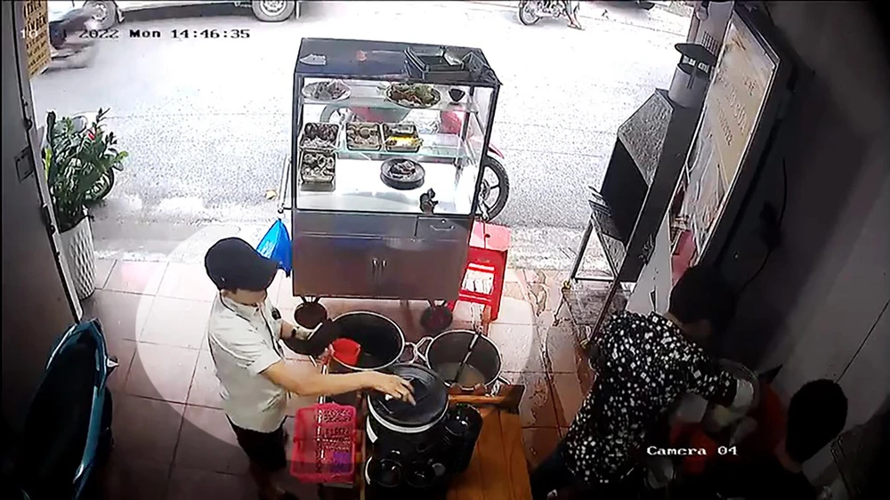 Người phụ nữ tranh thủ chủ quán quay lưng làm cơm thì lấy điện thoại. Ảnh chụp từ clip