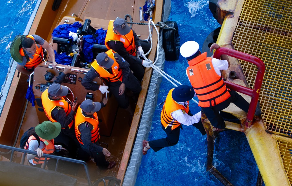 Cả lực lượng trên cano và trên nhà dàn phải lựa những lúc con sóng đẩy cano lên để hướng dẫn các thành viên trong đoàn công tác bám vào bậc thang và được dìu lên trên. Ảnh: NT