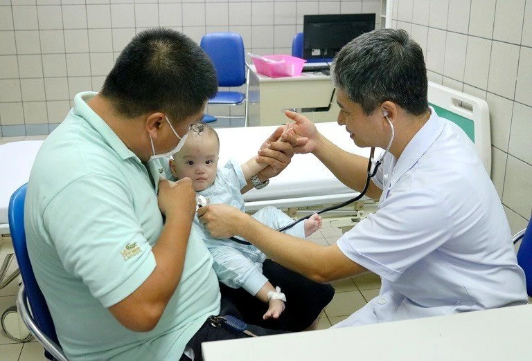 Bé An Chi trong vòng tay bố và bác sĩ Bệnh viện Bạch Mai. Ảnh: BVCC