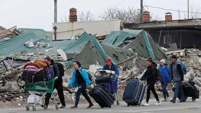 Người dân Ukraine mang theo đồ đạc đi qua một tòa nhà bị phá hủy ở Mariupol vào ngày 19-4. Ảnh: REUTERS