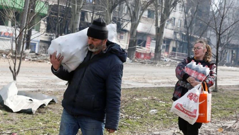 Người dân địa phương mang theo thực phẩm khi đi ngang qua một tòa nhà chung cư bị hư hại ở TP Mariupol, Ukraine, vào ngày 31-3. Ảnh: REUTERS