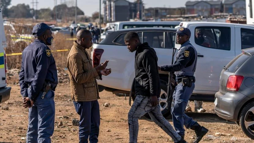 Cảnh sát dẫn một người đàn ông ra khỏi hiện trường vụ nổ súng tại quán bar ở Soweto, Nam Phi, ngày 10-7. Ảnh: AP